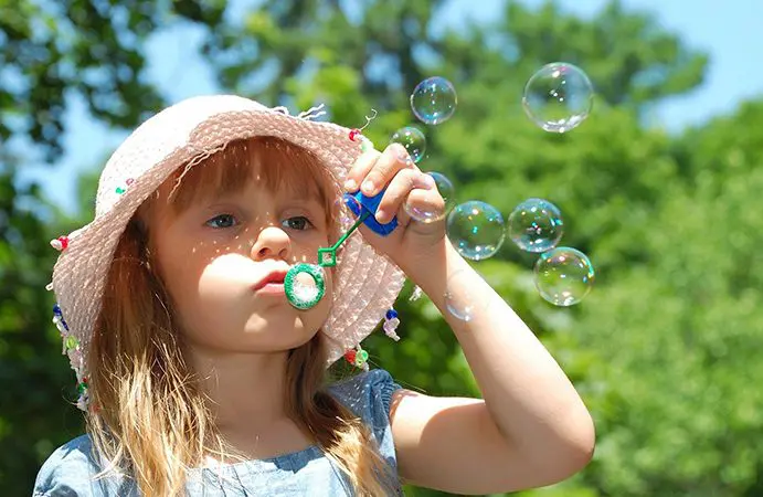 A little girl blowing bubbles with her toy.